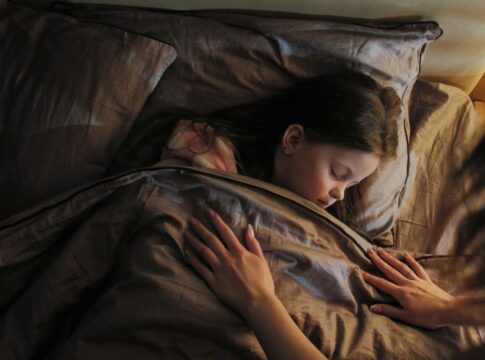 A child sleeps peacefully under a cozy blanket, with a parent tenderly tucking them in.