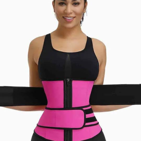 A woman is wearing a bright pink and black waist trainer belt over her workout attire. The belt features a zipper down the center and an adjustable strap.